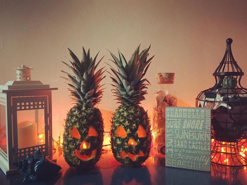 two Pineapple jack-o'-lantern on a shelf with candle holfder and sign 