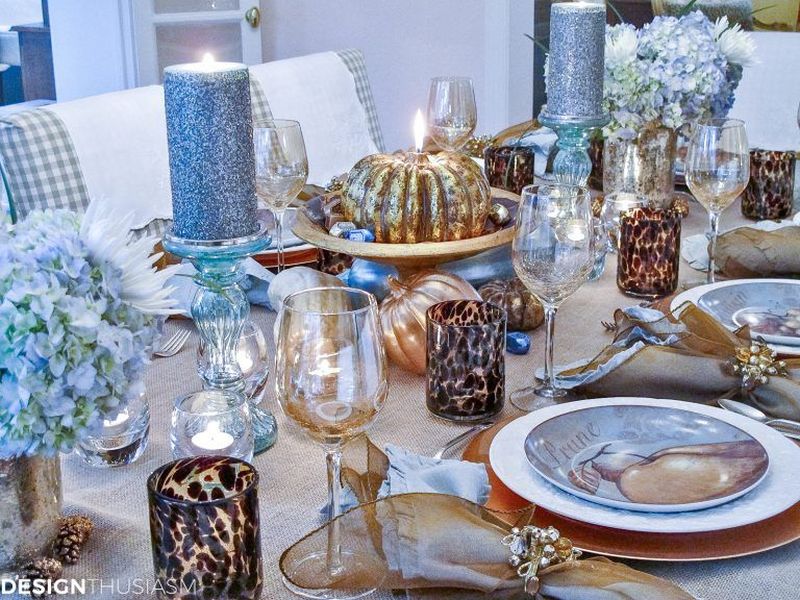 Thanksgiving table decor with gourds painted in metallic accents and have burlap tablecloth, hydrangea florals, glittered acorns