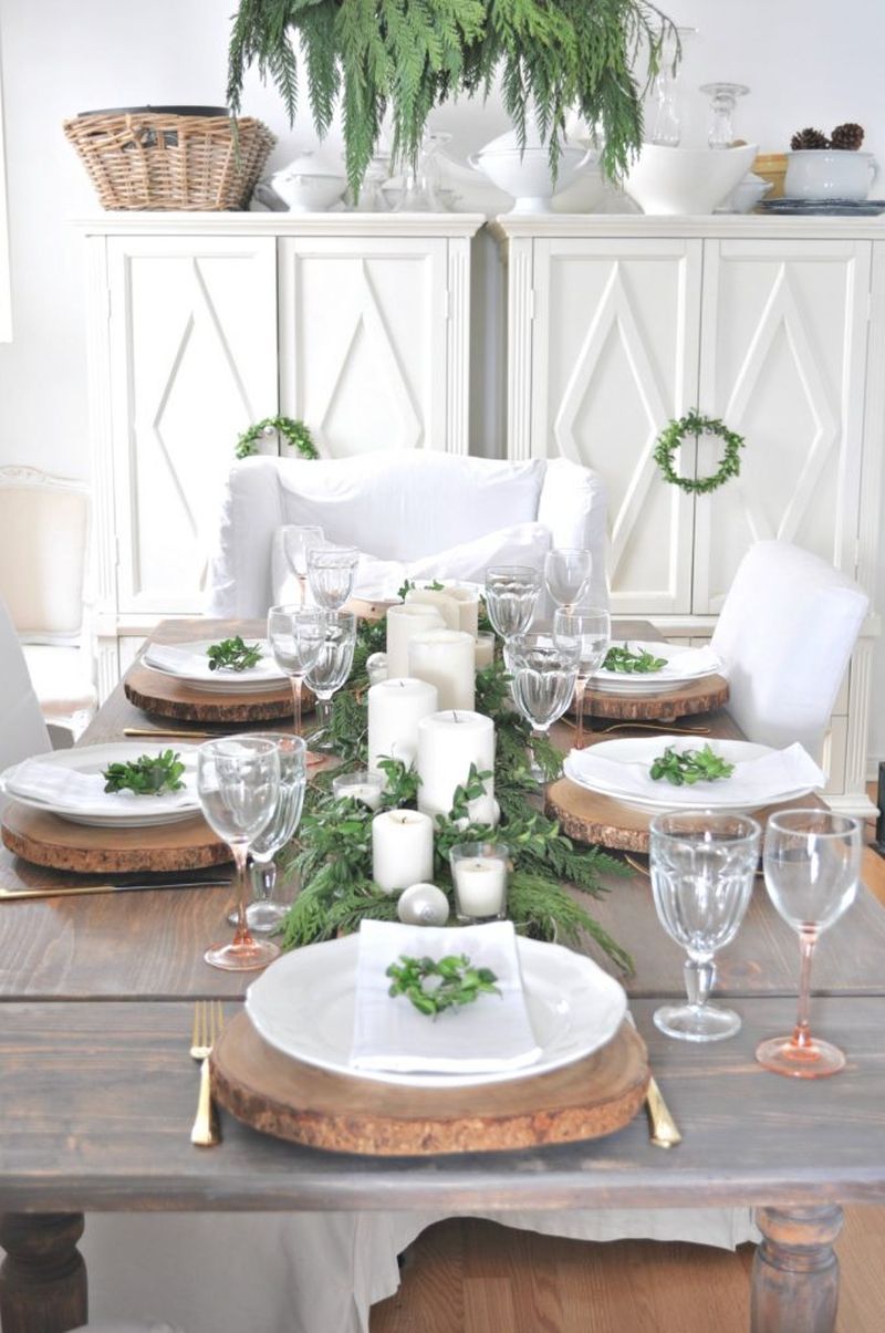 Christmas dining table decor with wood, greenery, gold cutlery, white plates, and candles 