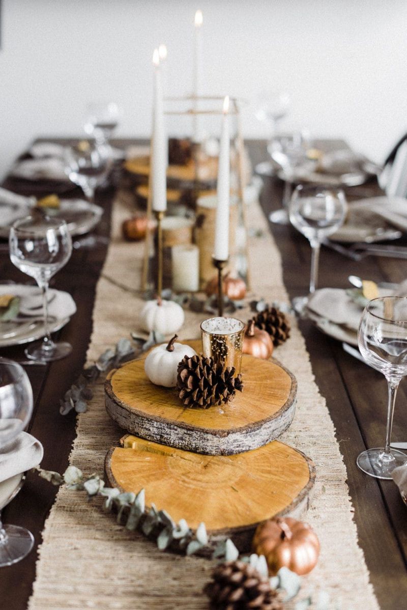 Rustic Thanksgiving table decor with round tree trunk slices, dried eucalyptus, pinecones, and tapered candles