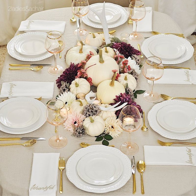 Thanksgiving table decked with un-ironed tablecloth, white plates and pumpkins, gold-rimmed glassware, napkins with gold embroidery, and whitened antlers