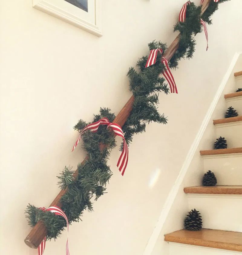 Pine cones placed on staircase steps and red ribbon tied to garland on hand rail 