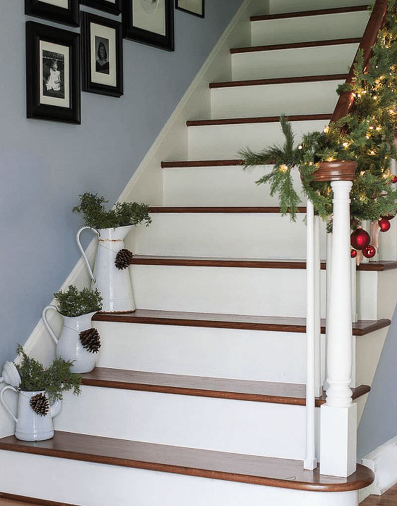 Planters with greenery and pine cones placed on white staircase steps 